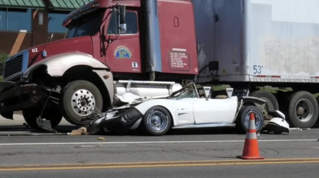 Crushed car under red truck on road scene